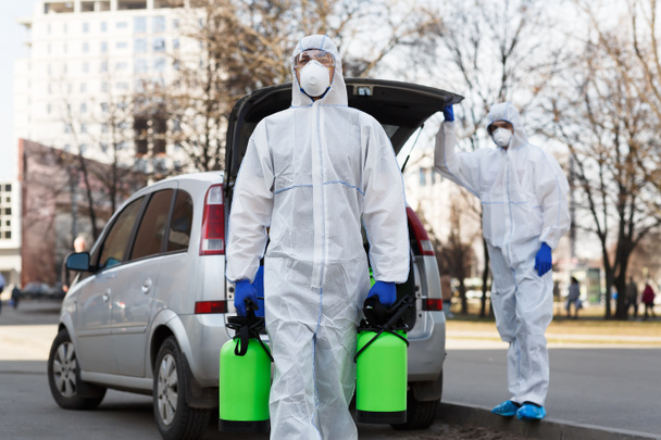 Muž v koronavirovém obleku nesoucí dezinfekční plyn - Fotografie, Obrázek