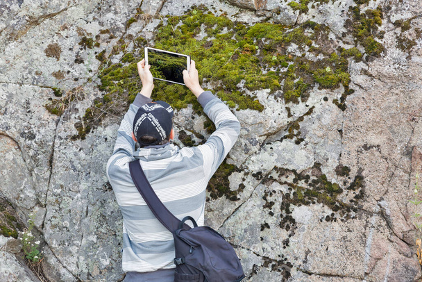 ZAPORIZHZHYA, UKRAINE - Kesäkuu 28, 2018: Mies ottaa kuvan sammalta kalliolla tabletilla aikana PhotoCamp Ukrainan valokuvaajat vuosikokous Khortytsia saarella
. - Valokuva, kuva