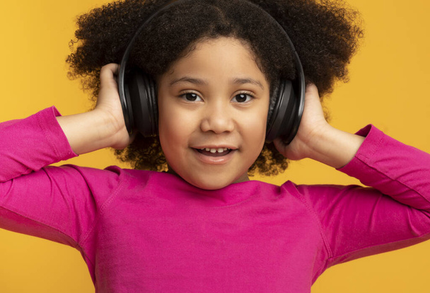 χαριτωμένο μικρό μαύρο κοριτσάκι σε ασύρματα ακουστικά πάνω από κίτρινο φόντο - Φωτογραφία, εικόνα