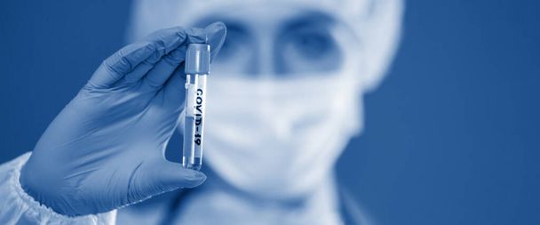Nurse holds a COVID-19 blood test tube. Doctor is wearing a mask and gloves to protect against infectious diseases. Coronavirus epidemic. Selected Focus. Close-up. Banner for web designe. - Photo, Image