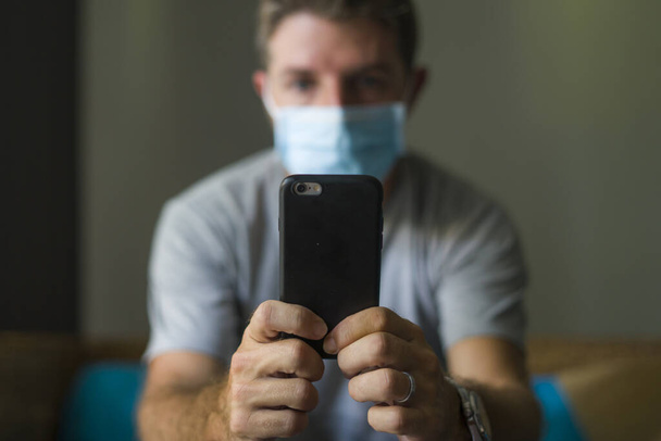 following online news on covid-19 virus pandemic - man with face mask in home quarantine lockdown checking internet information on the contagious disease scared and worried - Fotoğraf, Görsel