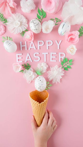 Hand holds a waffle cone with white paper flowers and white easter eggs with silver decor on pink background. Happy Easter concept. Long format for web - Foto, Imagem