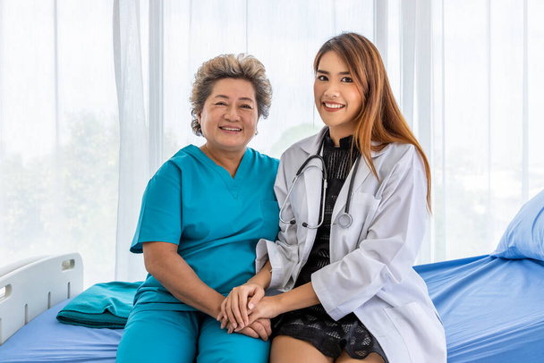 Azji lekarz trzymając starszych starszych kobiet pacjenta kobieta ręka siedzi na łóżku, aby pocieszać i motywować, patrząc w aparat - Zdjęcie, obraz