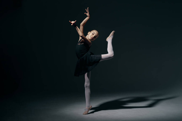 Beautiful girl ballerina dancing in light play and shadowson dark background - Photo, Image