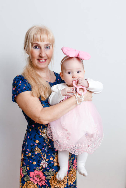 a retired woman holds a six-month-old baby in her arms on a white background - Foto, Imagen
