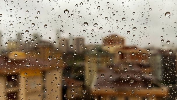 Raindrops on office window with blur grey sky background. Office window covered with closeup rain water. - 写真・画像