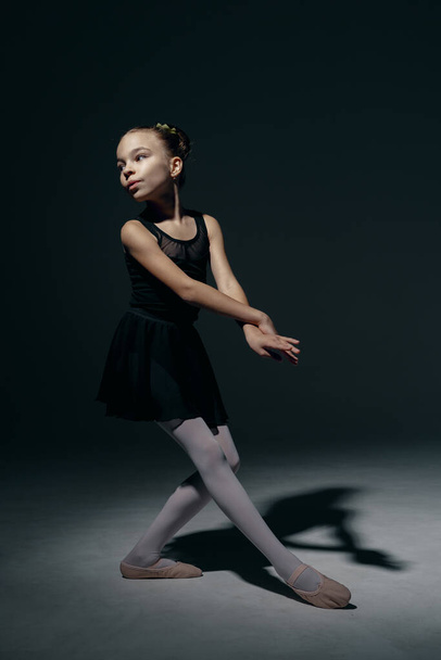 Beautiful girl ballerina dancing in light play and shadowson dark background - Photo, Image