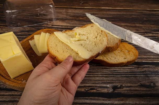 qualcuno spalma il burro sul pane tostato di grano fresco con un coltello, un piatto di burro di legno con burro e fette di formaggio su uno sfondo di legno. Da vicino.
 - Foto, immagini