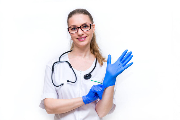 Protecting healthcare workers from infection. A female doctor puts on medical gloves on a white isolated background and smiles. Personal protective equipment before examination of patients - 写真・画像