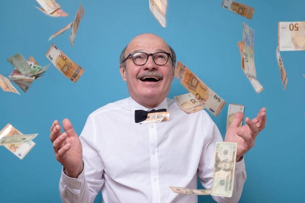 Vanhempi liikemies iloitsee menestyksestään ilmassa lentävien setelien kanssa
 - Valokuva, kuva