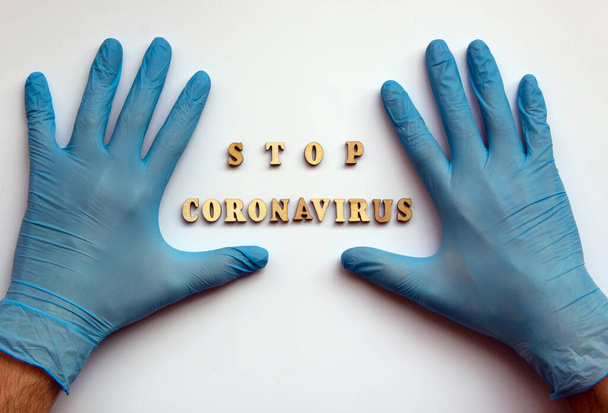 Mavi tıbbi eldivenli eller. Tahta harflerdeki ifade Coronavirus 'u durduruyor. Kirliliğe karşı koruma, virüsler, grip ve koronavirüs. Sağlık sigortası konsepti. Düz yat, boşluğu kopyala. - Fotoğraf, Görsel