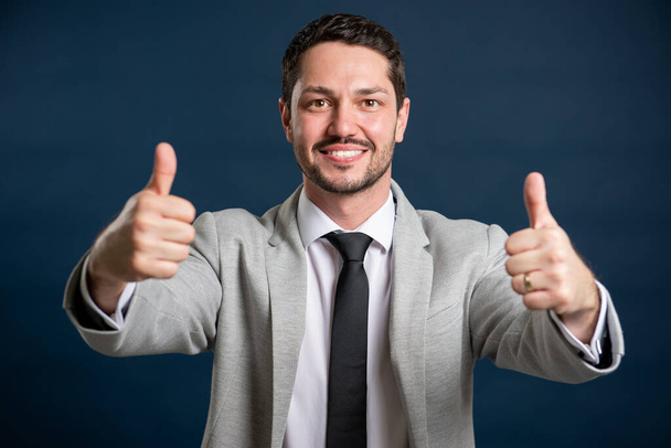 Портрет делового молодого привлекательного мужчины, показывающего большой палец вверх на синем фоне
 - Фото, изображение