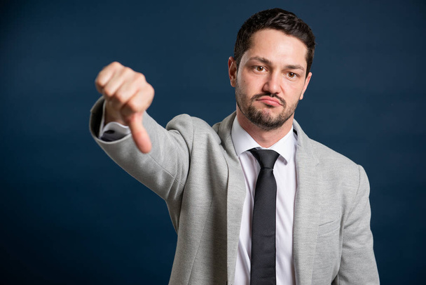 Portrét podnikání mladý pohledný muž ukazující palec dolů gesto na modrém pozadí - Fotografie, Obrázek