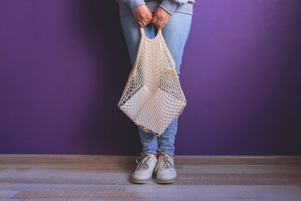 young woman in casual clothes holds a string bag with books against a purple wall and parquet floor - Foto, afbeelding