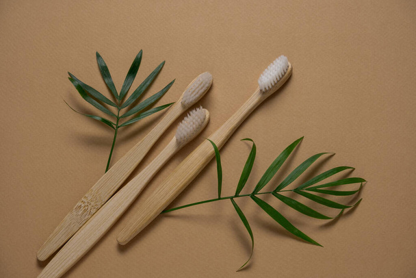 op view eco friendly wooden tooth brushes  and green tropical leaves layout on a brown background with copy space - Φωτογραφία, εικόνα