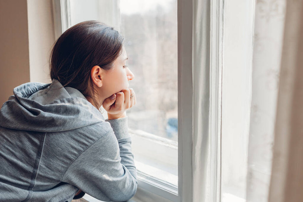 Isolatie thuis tijdens de coronavirus covid-19 pandemie. Een vrouw die naar het raam kijkt. Triest meisje blijft veilig thuis in quarantaine - Foto, afbeelding