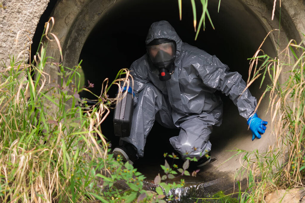 laboratory worker in protective suit and breathing apparatus crawls out of the pipe - Фото, зображення