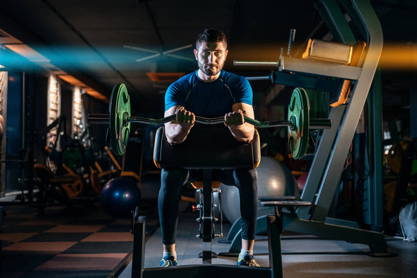 молодой спортсмен имеет физическую тренировку с штангой в современном тренажерном зале
 - Фото, изображение