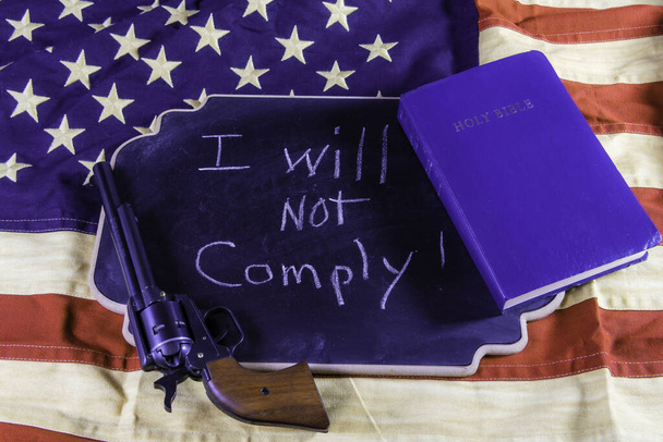 I will not comply written on small chalk board on American flag with hand gun and Bible - Фото, зображення