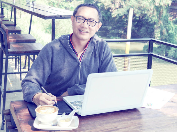 Azië middelbare leeftijd freelance werken met de muis pen op laptop in outdoor restaurant of cafe. - Foto, afbeelding