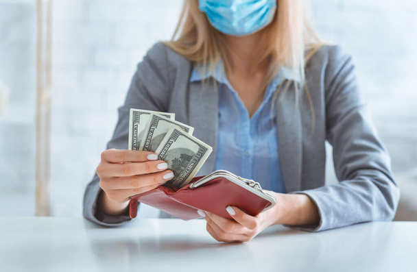 Woman in protective mask puts dollars in wallet - Φωτογραφία, εικόνα
