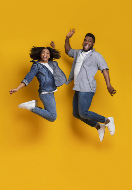 Ελευθερία. Χαρούμενο μαύρο ζευγάρι που πηδάει στον αέρα πάνω από κίτρινο φόντο - Φωτογραφία, εικόνα