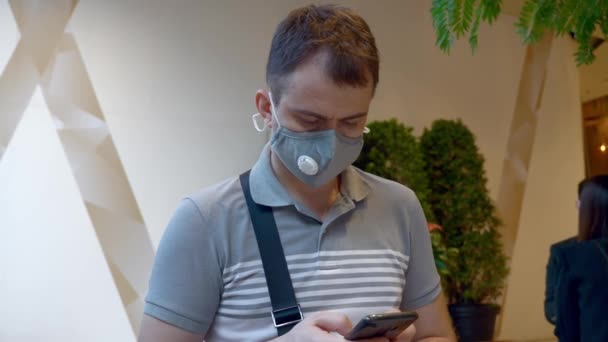 Hombre en Salud Cara Máscara Stand en el Salón de Negocios Uso del Edificio Smartphone
 - Metraje, vídeo