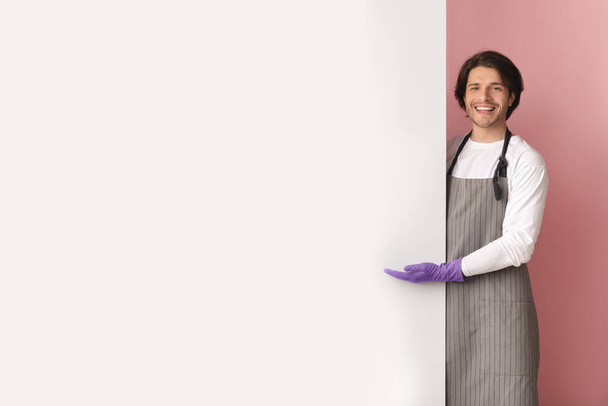 Promo de limpieza. Conserje masculino sonriente apuntando al espacio de copia en el tablero de anuncios blanco
 - Foto, Imagen