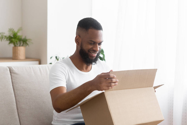 Online shopaholic. Glad african american man unpack parcel - Photo, Image