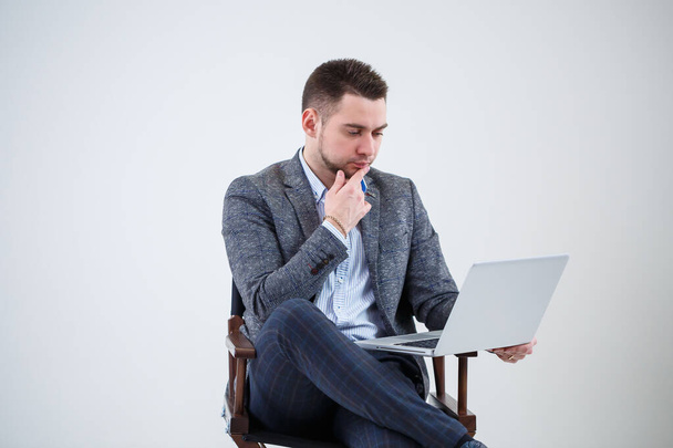 Мужчина-директор-бизнесмен, сидящий на стуле и изучающий документы. Он смотрит на экран ноутбука. Новый бизнес-проект
. - Фото, изображение