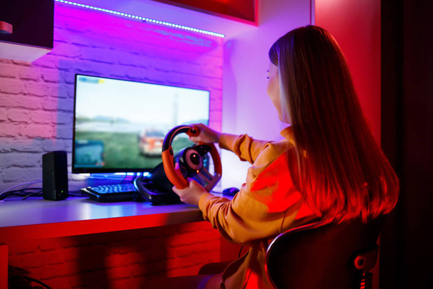 Tyttö gamer pelaa kilpaa tietokoneella. Hän käyttää ohjauspyörää. emotionaalinen pelata
 - Valokuva, kuva