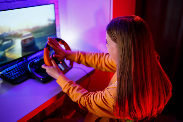 meisje gamer spelen racen op een computer. Ze gebruikt een stuur. emotioneel spel - Foto, afbeelding