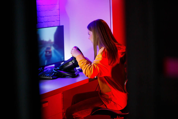 gamer κορίτσι παίζει αγωνιστικά σε έναν υπολογιστή. Χρησιμοποιεί τιμόνι. συναισθηματικό παιχνίδι - Φωτογραφία, εικόνα