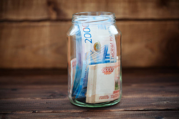 Geld in einem Glasgefäß auf einem hölzernen Hintergrund. Russische Banknoten.  - Foto, Bild