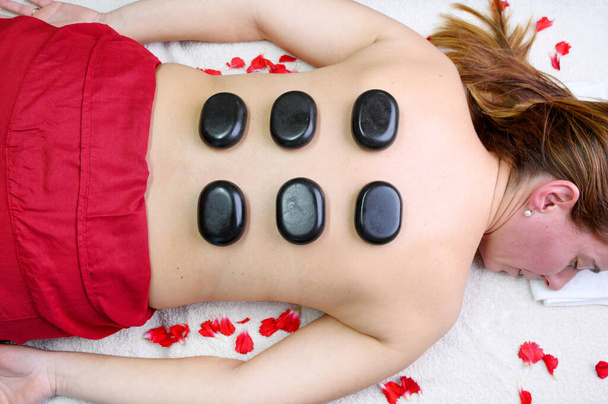 Tratamiento de piedra. Mujer joven tumbada en frente disfrutando de un masaje en el spa con piedras calientes en la espalda. Concepto de tratamiento de belleza
. - Foto, Imagen