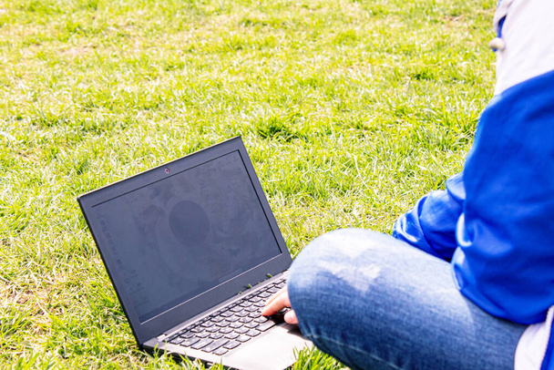草の上にノートパソコンを持った女の子。距離レッスン。オンラインレッスン。選択的焦点 - 写真・画像