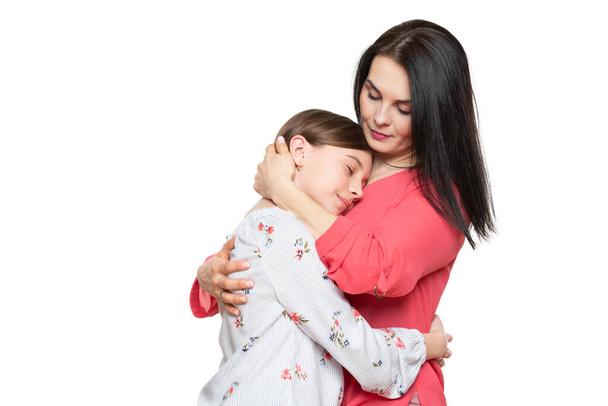 Waist up studio portrait of a young mother embracing her cute schoolgirl daughter. Happy smiling family background isolated over white background. - Foto, Imagen