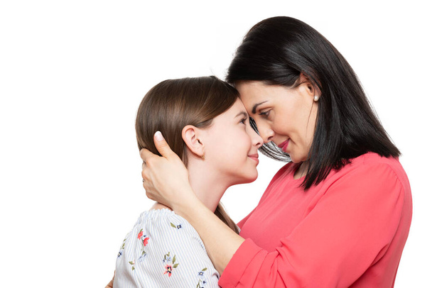 Waist up studio portrait of a young mother embracing her cute schoolgirl daughter. Happy smiling family background isolated over white background. - Photo, image