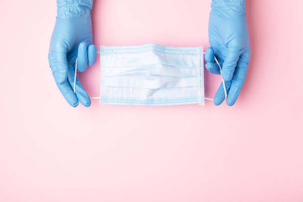 Kék kesztyűs kezek orvosi arcmaszkot mutatnak rózsaszín alapon. A vírusfertőzés elleni védekezésre irányuló megelőző intézkedések. - Fotó, kép