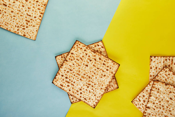 Pesah celebration concept - jewish Passover holiday. Background matzo on a yellow-blue background. View from above. Flat lay. Copy space. - Photo, Image