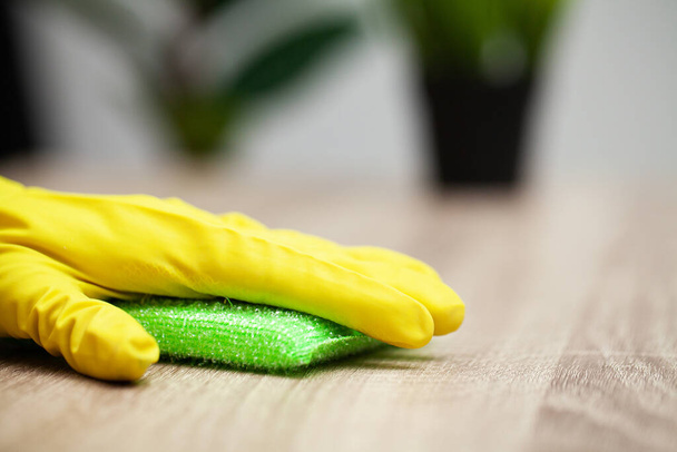 Закрытие рабочих рук, вытирающих пыль в офисе в жёлтых перчатках
 - Фото, изображение