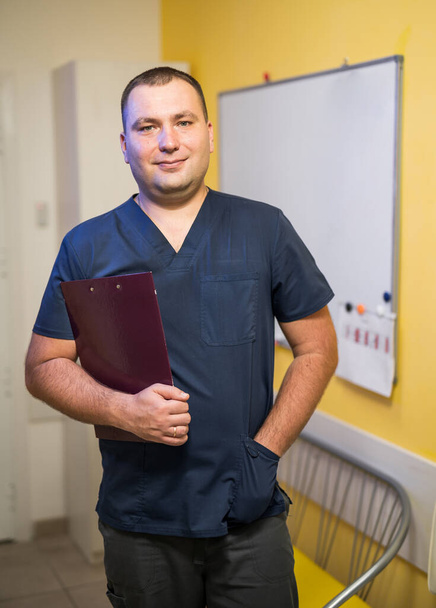 Male Doctor standing with folder at hospital. Whiteboard on backgound. - Foto, afbeelding