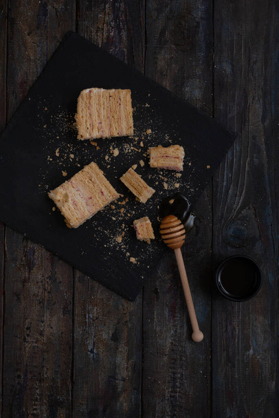 Sweet homemade layered honey cake on a black table with honey and crumbles - Foto, Imagem