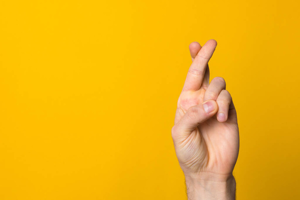 fingers crossed hope sign. close up man hand symbolising faith against yellow background - Φωτογραφία, εικόνα