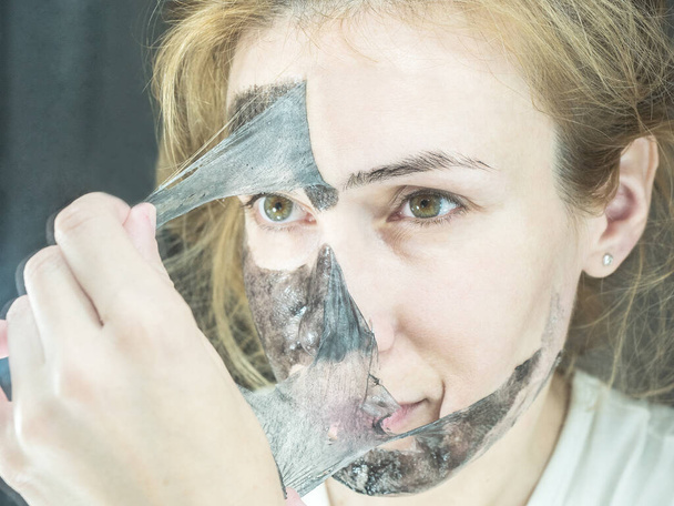 Blonde girl takes off from the face black thin transparent mask to clean pores - Photo, Image