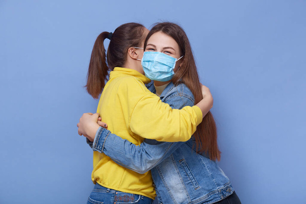 Studio shot of two young happy friends meeting each other during quarantine, wearing antibacterial masks, close contact, not sticking to rules, wearing casual clothes. People and health concept. - Photo, Image