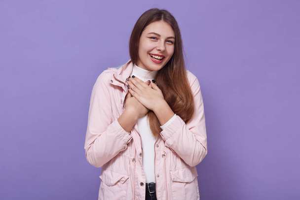 Portrait of positive adorable attractive cute female standing isolated over lilac background in studio, having folded arms, wearing cap and leather jacket, having beautiful smile. Youth concept. - Fotó, kép