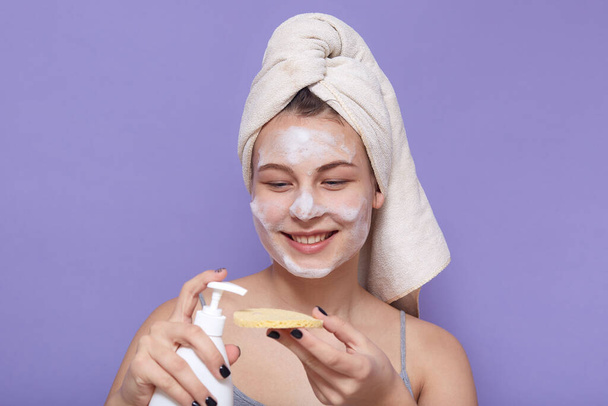 Portrait of smiling sincere beautiful young girl having spa day, clearing her skin, use cosmetological liquid, holding bottle with gel and sponge, having applied facial mask. Beauty concept. - Foto, imagen