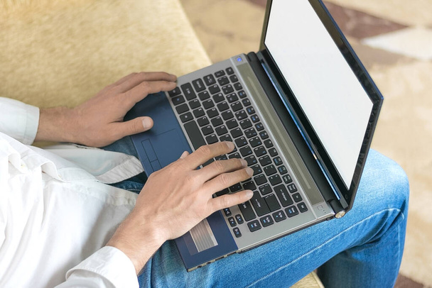  jovem homem de camisa branca e jeans azul trabalhando no laptop, escreve em notebook em home office sentado no sofá bege acolhedor Fique em casa, trabalho on-line, conceito de aprendizagem à distância
  - Foto, Imagem