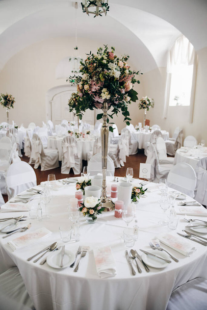 Belle table ronde de mariage pour les invités, décorée avec composition de fleurs, bougies, vaisselle, argenterie, menu, serviettes
 - Photo, image